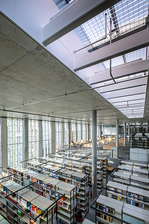 Innenansicht einer modernen Bibliothek mit hohen Decken, großen Fenstern und Bücherregalen in Reihen